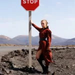 Femme en robe rouge appuyée sur un panneau stop.