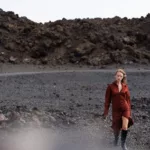 Femme marchant sur terrain rocheux en robe rouge.